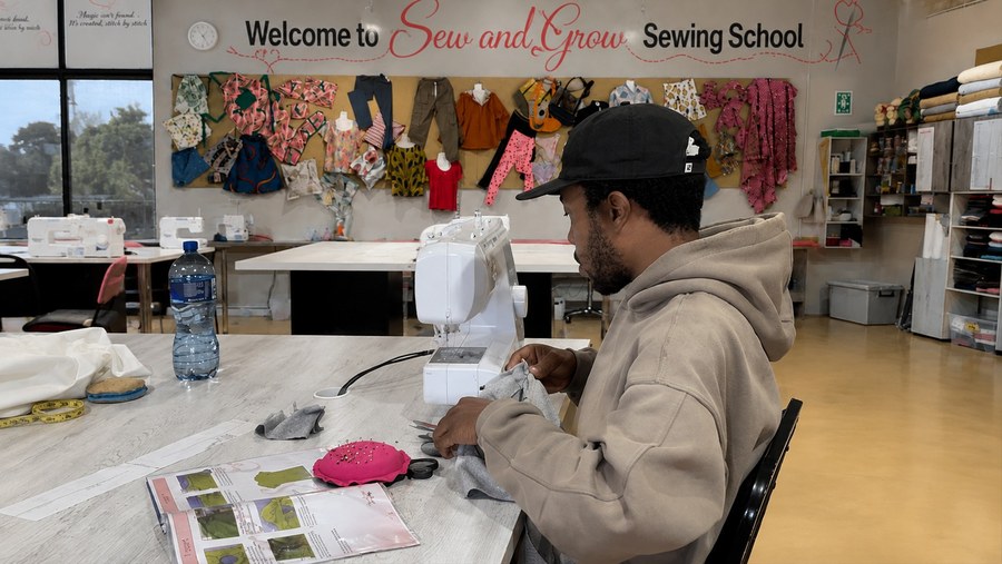 A man learning to sew at his machine under the welcome sign