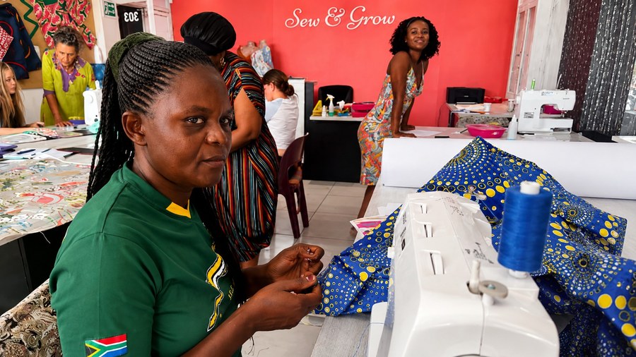 A student hand-threading at her machine with African-print fabric