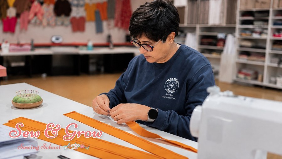 A student hand-stitching orange fabric in the studio